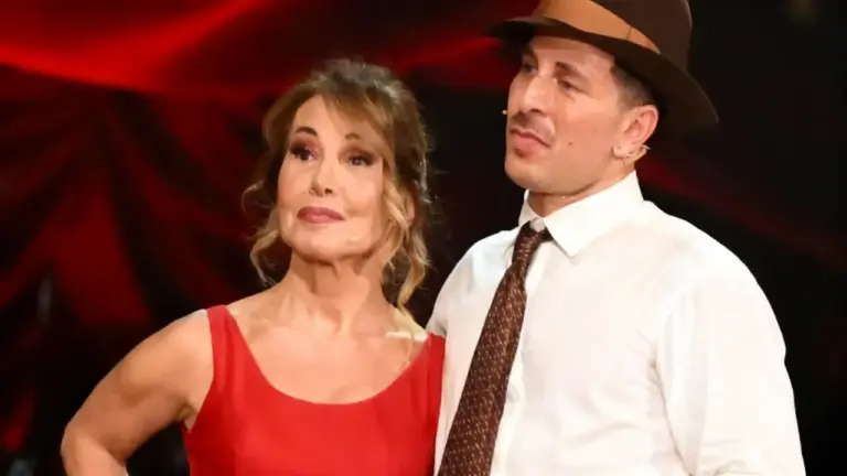 Due persone sul palco di uno show televisivo, una con abito rosso e l'altra con camicia bianca e cappello