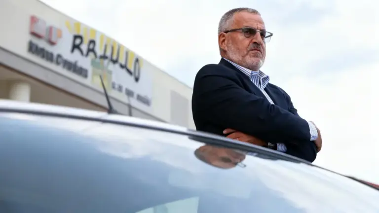 Un uomo in piedi accanto a un'auto con le braccia conserte, in un contesto urbano