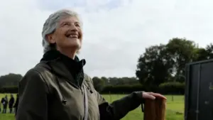 Una donna anziana sorride all'aperto in un paesaggio verde