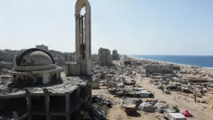 Edifici distrutti e tende in un'area costiera, con costruzioni in rovina sullo sfondo