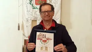 Una persona tiene una targa commemorativa davanti a uno stendardo araldico