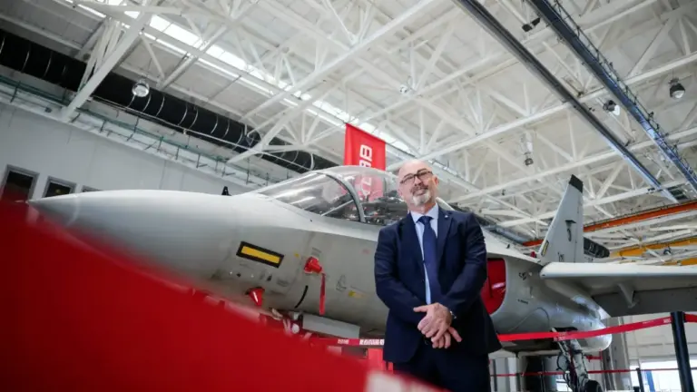 Persona in posa accanto a un aereo militare in un hangar industriale