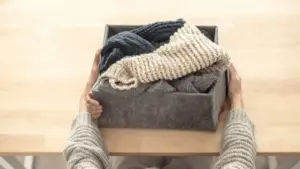 Una persona tiene una scatola di feltro con maglioni di lana piegati su un tavolo chiaro