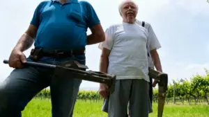Due persone in piedi in un vigneto con strumenti agricoli in mano