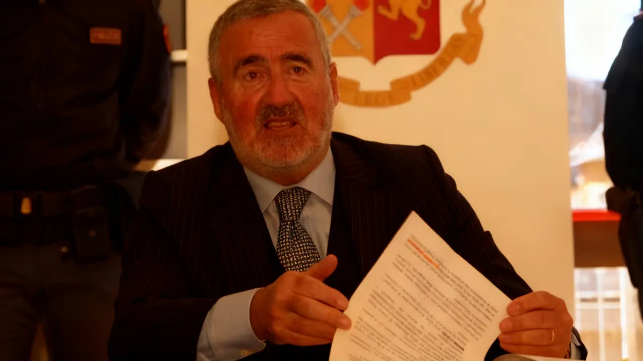 Un uomo in abito scuro tiene un documento durante una conferenza stampa.