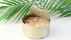 Scatoletta di tonno aperta su sfondo chiaro con foglie verdi