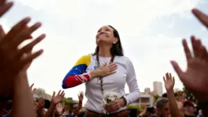 Una persona tra la folla con la mano sul petto e in mano un mazzo di fiori bianchi