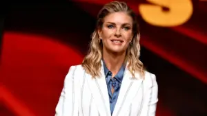 Una donna sorridente in primo piano su sfondo rosso durante un evento televisivo.