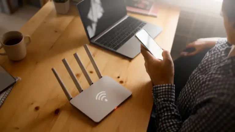 Persona seduta a una scrivania con smartphone, laptop e router Wi-Fi acceso