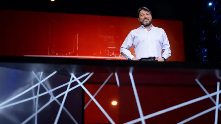 Un uomo in piedi su un palco con sfondo rosso e luci scenografiche