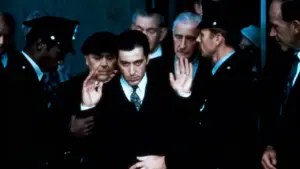 Un uomo in abito scuro con le mani alzate, circondato da altre persone in divisa