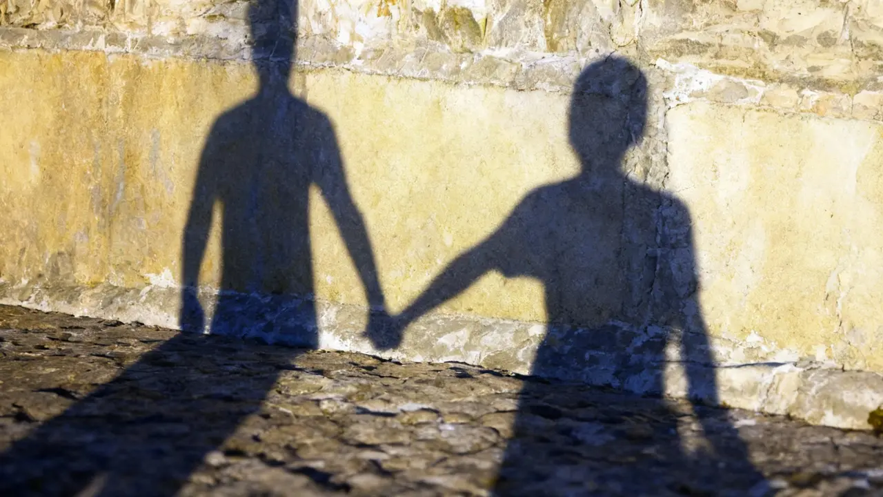 Ombre di due persone che si tengono per mano su un muro di pietra