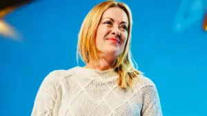 Una donna sorride davanti a uno sfondo blu, indossando un maglione chiaro