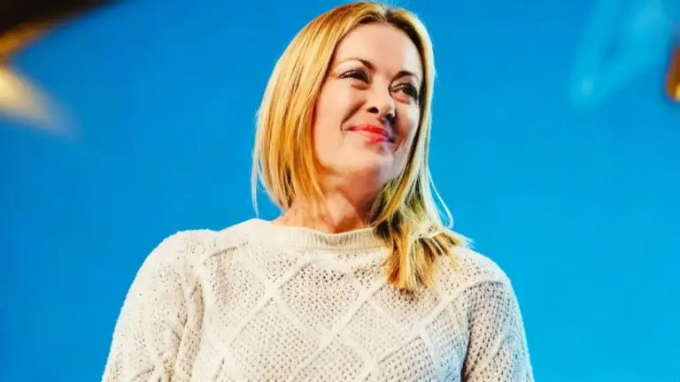 Una donna sorride davanti a uno sfondo blu, indossando un maglione chiaro