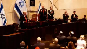 Una persona parla davanti a un podio nella Knesset, mentre altri applaudono.