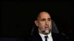 Un uomo seduto su una panchina durante una partita di calcio, con espressione seria