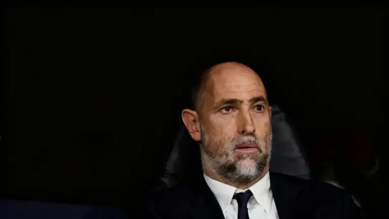 Un uomo seduto su una panchina durante una partita di calcio, con espressione seria