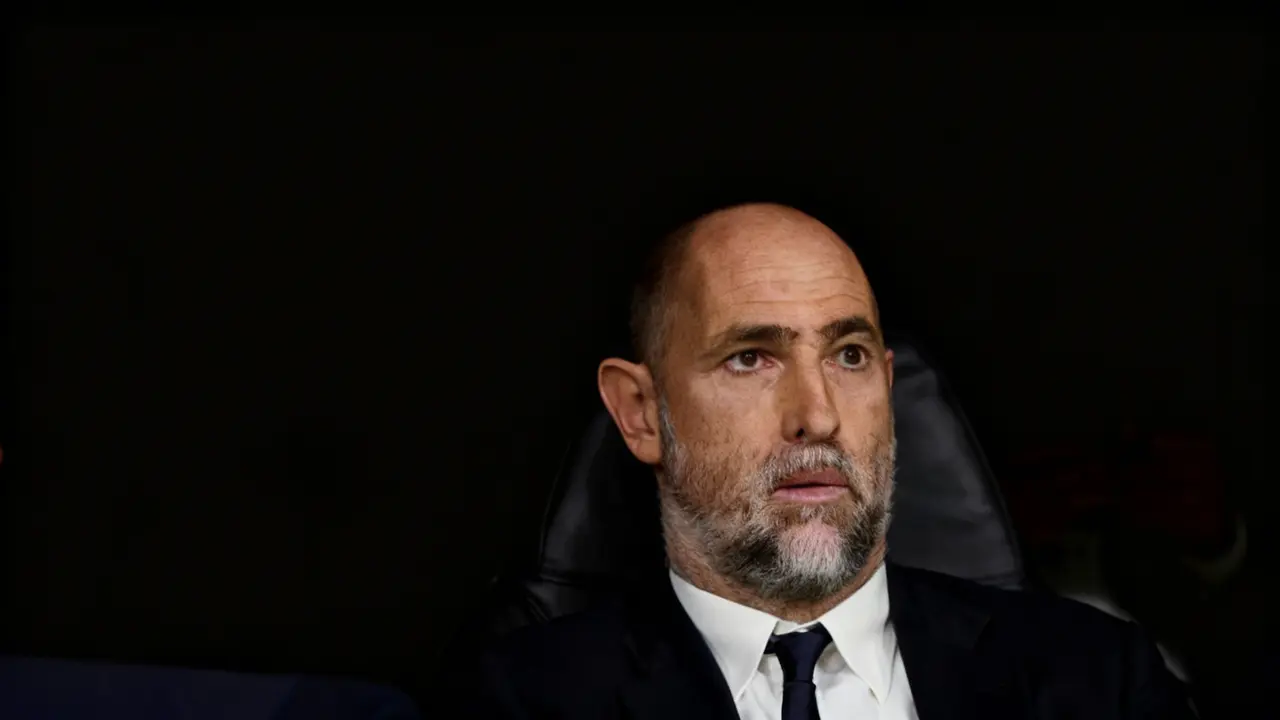 Un uomo seduto su una panchina durante una partita di calcio, con espressione seria