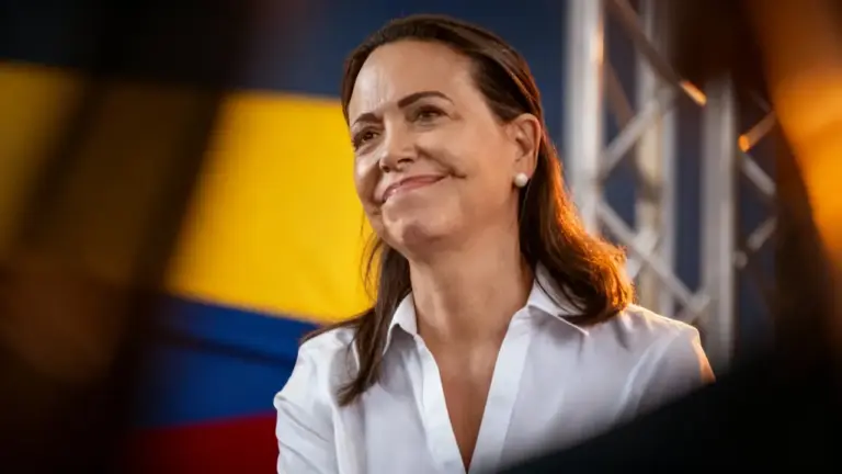 Una donna con espressione sorridente davanti a una bandiera colorata, in un contesto formale