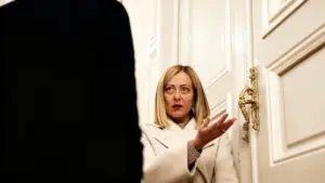 Una donna in cappotto chiaro parla con una persona di fronte a una porta elegante