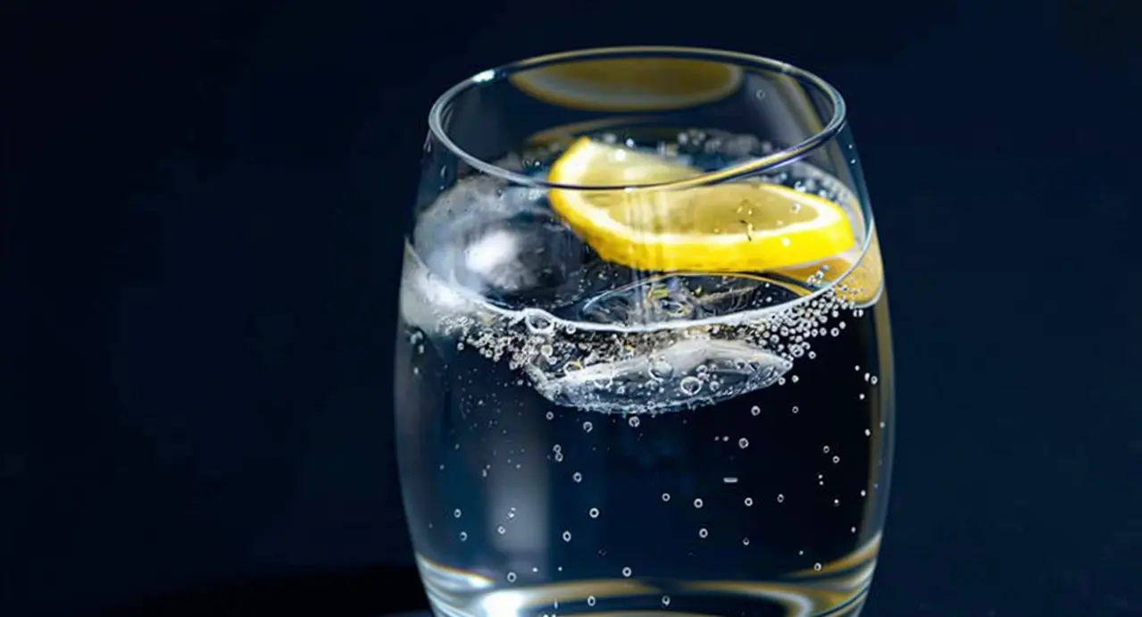 Bicchiere di acqua frizzante con ghiaccio e una fetta di limone su sfondo scuro