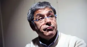 Un uomo con occhiali trasparenti e capelli grigi in un ambiente interno