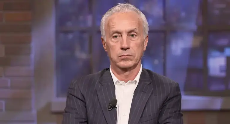 Una persona matura in abito scuro durante un'intervista televisiva o dibattito.