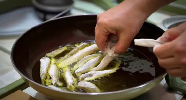 Mani che immergono filetti infarinati in una padella con olio caldo