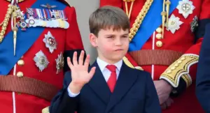 Un bambino in abito formale saluta accanto a figure in uniformi cerimoniali decorate