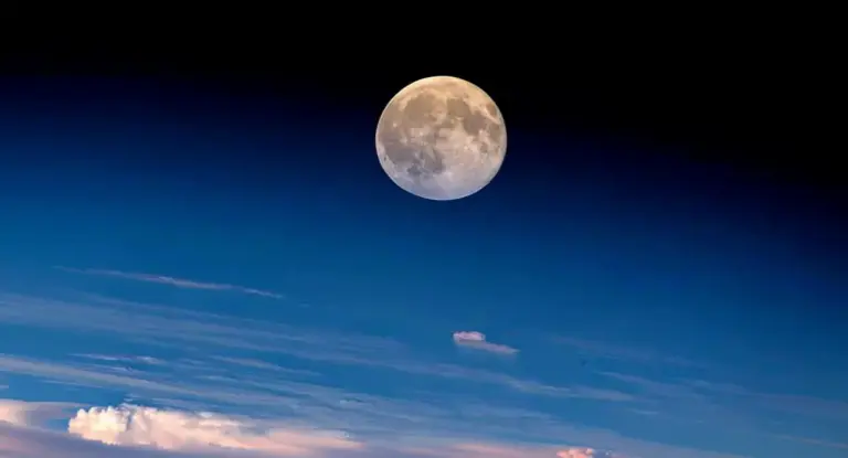 La Luna piena sopra l'atmosfera terrestre con nuvole all'orizzonte