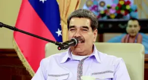 Una persona parla al microfono durante un intervento ufficiale con una bandiera sullo sfondo