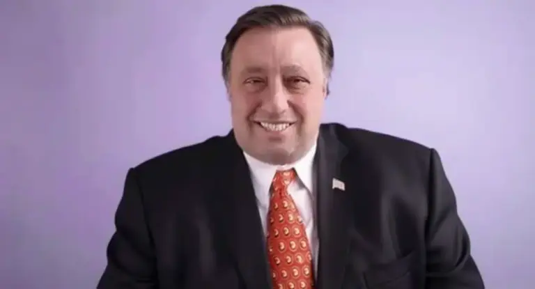 Un uomo in giacca e cravatta sorride davanti a uno sfondo viola