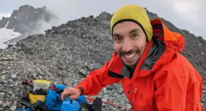 Una persona sorride in montagna indossando abbigliamento da trekking arancione