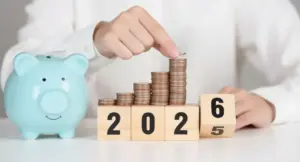 Mano che impila monete accanto a salvadanaio e blocchi con l'anno 2026